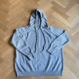 Ljusgrå hoodie med huva och snörning - En stilren ljusgrå hoodie med huva och snörning. Tröjan har långa ärmar, ribbade muddar och är tillverkad i ett mjukt material som känns skönt mot huden. Perfekt för en avslappnad look och enkel att matcha med jeans eller joggers. Nypris 600kr