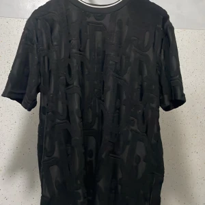 Svarta shorts och t- Shirts ö lohpåoim från Dior med struktur - Svarta shorts från Dior i 100% bomull med unik strukturerad yta och diskret mönster. De har elastisk midja med snörning för skön passform. Perfekta för dig som vill ha något stilrent men ändå med en twist, använd 3 gånger bara , nästan helt ny.