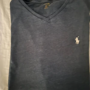 Mörkblå v-ringad t-shirt Polo Ralph Lauren - Snygg mörkblå t-shirt från Polo Ralph Lauren med klassisk v-ringning och broderad logga på bröstet. T-shirten är i bomull och har en normal passform, perfekt för en clean och stilren look.