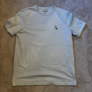 Vit t-shirt med tryck från H&M - Vit t-shirt från H&M i bomull med regular fit. På bröstet finns ett litet tryck med en fågel på en klippa och på ryggen ett större tryck med en fyr och texten 'FRANCE'. Rund hals och korta ärmar. Perfekt för dig som gillar clean stil med coola detaljer.