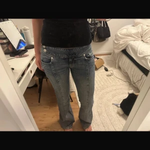 Lågmidjade bootcut jeans med snörning - Säljer ett par blå jeans med låg midja och bootcut-ben. Jeansen har cool snörning framtill, dubbla knappar och klassiska fickor. De är i en ljus tvätt och har en avslappnad, lite loose passform. Perfekta för dig som gillar retrovibbar och streetstyle.