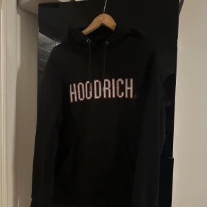 Svart HOODRICH hoodie med tryck - Svart hoodie från HOODRICH med stort vitt och rött tryck på bröstet. Storleken är M men sitter mer som en S. Säljs pga den ej passar min stil längre. 