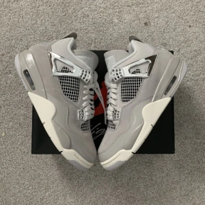Nike Air Jordan 4 Retro Metallic Silver - Nike Air Jordan 4 Retro i grått och silver med coola metallic-detaljer. Ovandel i mocka och syntet, meshpaneler och vita snören. Snygg platt sula och ikonisk Jumpman-logga undertill. Perfekta sneakers för dig som vill sticka ut med stilrena vibes de är helt nya.
