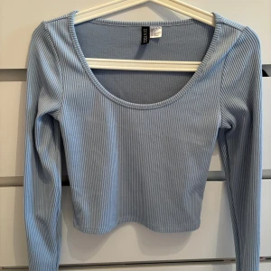 Ljusblå ribbad långärmad topp  - Supersnygg ljusblå långärmad topp från Divided med ribbat tyg och rundad urringning. Modellen är lite croppad och har smala ränder i tyget som ger en fräsch och modern känsla.
