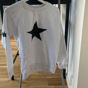 Vit sweatshirt med svarta stjärnor Just Rhyse - Säljer en vit sweatshirt från Just Rhyse i storlek M. Tröjan har svarta stjärnor tryckta på bröstet och ena ärmen, samt ribbade muddar vid hals, ärmslut och nederkant. Perfekt för dig som gillar streetstyle och grafiska detaljer.