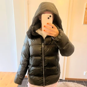 Grön pufferjacka från Massimo Dutti - Säljer en grön pufferjacka från Massimo Dutti med  huva och dragkedja framtill. Jackan har defekt på höger armbåge men går att fixa med tejp. Perfekt för kalla dagar och riktigt snygg.