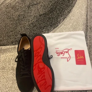 Christian Louboutin svarta sneakers - Snygga svarta sneakers från Christian Louboutin i mocka med klassisk röd sula och svarta snören. Skorna har rund tå och platt sula, perfekt för dig som vill ha en lyxig och stilren look. Kommer med dustbag och äkthetskort.