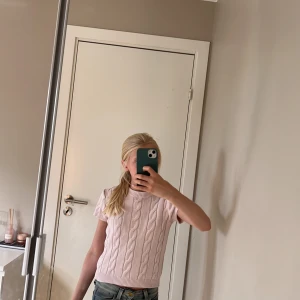 Ljusrosa stickad tröja Gina Tricot - Supersöt ljusrosa stickad tröja från Gina Tricot med korta ärmar och klassiskt flätmönster. Rund hals och ribbade kanter ger en chill vibe. Perfekt till jeans eller kjol för en fräsch look. Passar dig som gillar mjuka pasteller och enkel stil.