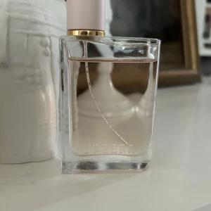 Burberry Her parfym 50ml - Säljer en Burberry Her parfym i en stilren, transparent glasflaska med ljusrosa lock och gulddetalj. Flaskan rymmer 50ml och har en elegant, modern design med Burberry-loggan ingraverad längst ner. Doften är fräsch och feminin.
