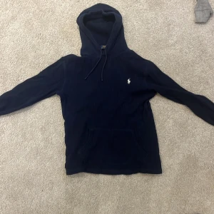 Mörkblå hoodie från Polo Ralph Lauren - Säljer en mörkblå hoodie från Polo Ralph Lauren med broderad logga på bröstet. Tröjan är ribbad, har huva med snörning och en stor magficka. Tröjan är i storlek S men passar runt 160