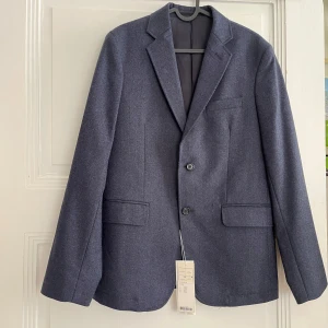 Blå ullkavaj från ARKET - Snygg blå kavaj från ARKET i mjuk ullflanell. Klassisk modell med två knappar, tre fickor fram och knappar vid ärmslut. Fodrad insida och stilren passform, perfekt för dig som gillar en tidlös look.