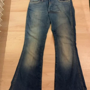 Blå bootcut jeans från Wrangler - Säljer ett par klassiska blå bootcut jeans från Wrangler med snyggt slitna detaljer och kontrastsömmar. Tyvärr är de för små för mig och för korta. Storleken är W26 L32. Jeansen är i bra skick och har inga hål någonstans!💕