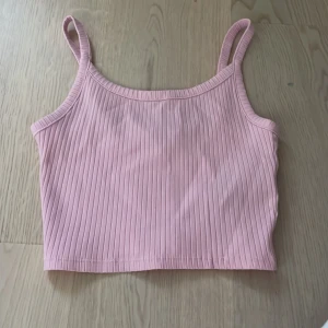 Ribbad rosa linnetopp från FB Sister - Supersöt ljusrosa ribbad linnetopp från FB Sister. Croppad modell med smala axelband och stretchigt material som sitter snyggt. Perfekt till jeans eller kjol för en fräsch look. Enkel och stilren design som är lätt att matcha.