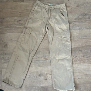 Beige cargobyxor från Samsa Young - Snygga beige cargobyxor från Samsa Young med raka ben och flera praktiska fickor på sidorna. Byxorna har normal passform och är tillverkade i mjuk bomull, perfekta för en avslappnad och cool stil.