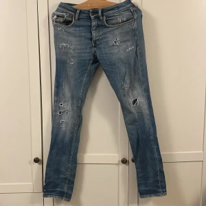 Blå slitna jeans från Jack & Jones storlek 29 32 - Säljer ett par blå jeans från Jack & Jones med coola slitningar och hål på benen för en edgy look. Klassisk femficksmodell med knappgylf och broderad logga på insidan av midjan. Jeansen har en rak passform och är tillverkade i bomull.