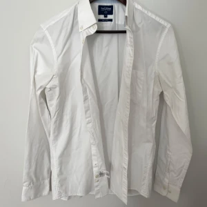 Vit skjorta från T.M. Lewin, M - Klassisk vit skjorta från T.M. Lewin i storlek M. Skjortan har lång ärm, knappar framtill och en stilren krage. Tillverkad i bomull och är lätt att stryka. Perfekt för dig som gillar en clean och enkel look.