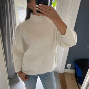 Vit stickad polotröja i loose fit - Vit stickad polotröja med hög ribbad krage och avslappnad, loose passform. Tröjan har raka, lite kortare ärmar och två små smuts fläckar på framsidan som säkert går bort i tvätten