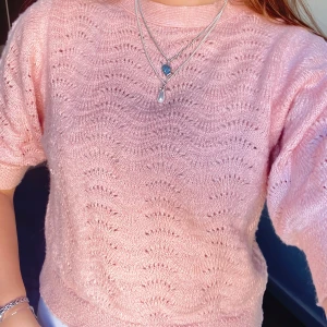 Ljusrosa stickad tröja med mönster - Superfin ljusrosa stickad tröja med korta ärmar och vågigt hålmönster över hela. Tröjan har en rund halsringning och ribbade muddar vid ärmslut och nederkant. Perfekt för hösten