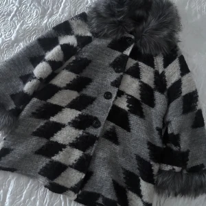 Italiensk rutig pälsjacka med knappar - Snygg och unik pälsjacka från Italien med rutigt mönster i svart, grått och vitt. Jackan har stora knappar framtill, fluffig fuskpälskrage och pälsdetaljer vid ärmsluten. Perfekt för dig som vill sticka ut med en statementjacka i vinter.