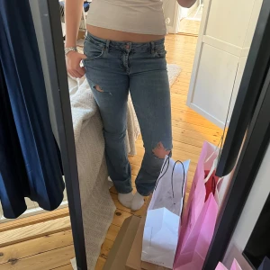 Blå jeans med slitningar - Snygga blå jeans med slitningar på knäna. De har en klassisk femficksdesign och en lågmidjad passform. Perfekta för en avslappnad stil.