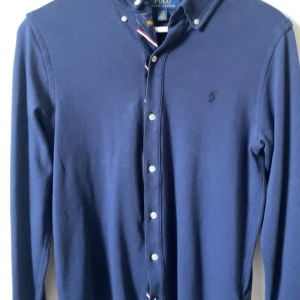 Blå skjorta från Ralph Lauren - Säljer en stilren blå långärmad skjorta från Ralph Lauren med knappar och broderad logga på bröstet. Perfekt för en klassisk look. 