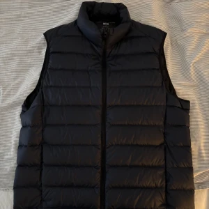 Marinblå dunväst från Uniqlo - Säljer en stilren marinblå dunväst från Uniqlo. Västen har en dragkedja framtill och är perfekt för lager-på-lager under kyligare dagar. Den är lätt och smidig att bära med sig. Passar både till vardags och mer avslappnade tillfällen. Jackan är även använd under 3 gånger och är i toppskick, undrar du något så är det bara att höra av dig👍