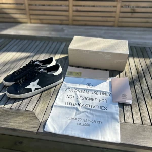 Golden goose - Snygga svarta sneakers från Golden Goose med en vit stjärna på sidan. Skorna har en klassisk design med snörning och en vit sula. Perfekta för en stilren look.