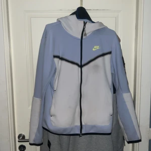 Ljusblå och vit jacka från Nike - Säljer en snygg ljusblå och vit jacka från Nike med dragkedja och huva. Jackan har ett stilrent märke i gult på bröstet och svarta detaljer längs dragkedjan och ärmarna. Negativa saker: Den har en grå fläck som jag e osäker om de går o tvätta bort. Men kommer tvätta innan den skickas iväg på förhoppning att fläcken försvinner 😊 