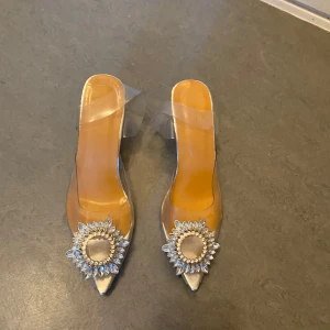 Transparenta klackskor med strassdetaljer - Snygga transparenta klackskor med spetsig tå och glittrande strassdetaljer framtill. Skorna har en klar blockklack och en stilren design som passar perfekt för festliga tillfällen. De är i ny skick använda en gång. De är från Shein storlek 35-36