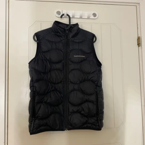Svart dunväst från Peak Performance - Snygg svart dunväst från Peak Performance med dragkedja framtill. Perfekt för kyliga dagar och ger en sportig look. Västen har en hög krage och är quiltad för extra värme. Storlek 160 och köpt från kids brandstore, pris går att diskutera 🥰 bara skriv vid frågor eller funderingar☺️ 