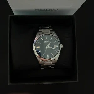 Silverfärgad klocka från Seiko - Elegant Seiko-klocka i silver med en stilren mörkblå urtavla. Klockan har ett datumfönster och en klassisk länkarmband i metall. Den är vara använd 1 gång vilket gör att den är som ny. Extra länkar medföljer! DM för mer bilder eller info💌