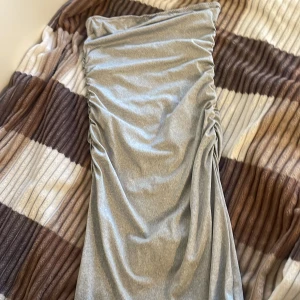 Grå klänning  - Snygg grå  klänning  med rynkade detaljer på sidorna. Klänningen har en elegant och stilren design som passar perfekt för olika tillfällen. Materialet ser mjukt och bekvämt ut.