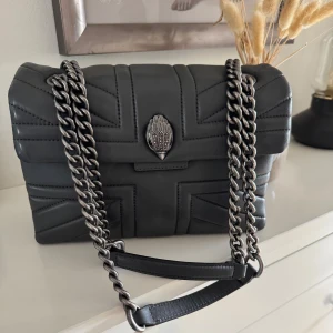 Väska från Kurt Geiger - Snygg grå väska från Kurt Geiger i skinn med kedjedetaljer. Väskan har en elegant design med ett dekorativt emblem på framsidan och en praktisk insida.  Väskan går borde att bära under axeln eller som en axelremsväska💛💛