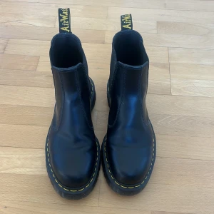 Svarta Chelsea boots från Dr. Martens - Snygga svarta Chelsea boots från Dr. Martens med den klassiska gula sömmen och dragflik med logga. Tillverkade i slitstarkt skinn med en robust sula som ger bra grepp. Perfekta för både stad och natur. Använda vid fem tillfällen. Nypris 2 300 kr