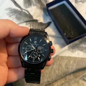 Svart klocka från Poedagar - Snygg svart klocka från Poedagar med metallarmband och flera urtavlor. Klockan har en stilren design med tydliga siffror och visare. Perfekt för den som gillar en elegant och modern stil.
