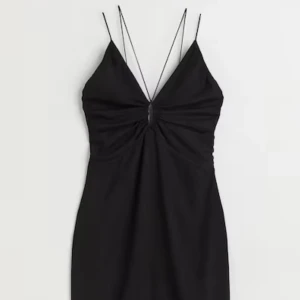 Svart klänning med smala axelband - Snygg svart klänning med smala axelband och djup v-ringning. Perfekt för en kväll ute eller en speciell tillställning. Klänningen har en figurnära passform och är tillverkad i ett mjukt material som ger en elegant look.