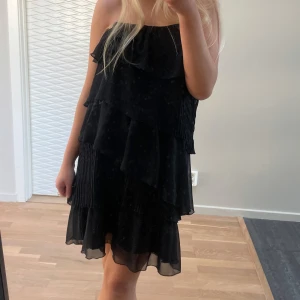 Svart  klänning - Snygg svart klänning med volanger. Perfekt för en stilren look. Klänningen har en luftig passform vilket gör den bekväm och lätt att bära.