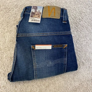 Blå jeans från Nudie Jeans - Säljer ett par snygga blå jeans från Nudie Jeans. De har en klassisk femficksdesign och är tillverkade i ekologisk bomull. Perfekta för en avslappnad stil med en modern touch.