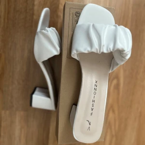 Vita sandaler med klack  - Stilrena vita sandaler med en fyrkantig klack och rynkad remdesign. Perfekta för en elegant look. Sandalerna har en öppen tå och är tillverkade i syntetmaterial. Storlek 39 men passar 38 också!!