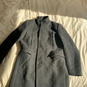 Grå kappa - Elegant grå kappa med hög krage och knäppning framtill. Den har en figursydd passform och långa ärmar. Perfekt för kyligare dagar.