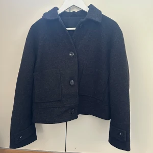 Svart kappa från 157 - Säljer en stilren svarta kappa från 157. Jackan har stora knappar framtill och två praktiska fickor. Perfekt för kyligare dagar med sin klassiska design och bekväma passform. Jackan är i nyskick då den aldrig kommit till användning. Nypris 400kr säljer 200kr. Priset går att diskutera 🥰