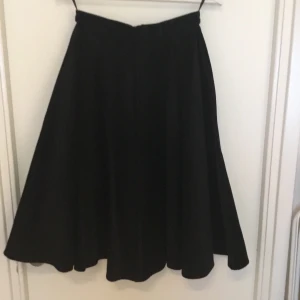 Svart kjol i manchester, Hell Bunny XS - Svart kjol i manchester (100% bomull )från märket Hell Bunny. Storlek: XS UK 8.  Fickor i sidorna, stängs med dragkedja och knapp i bak. Midja: ca 33x2 cm. Längd: 69 cm. Helt ny och oanvänd med alla lappar kvar. En extra knapp medföljer.