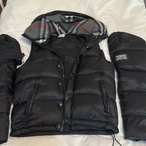 Svart pufferjacka/väst från Burberry - Säljer en snygg svart pufferjacka/väst från Burberry med avtagbara ärmar.Strl L. Jackan är väldigt skön och perfekt nu för våren. Jackan passar M/L Priset är ej hugget i sten!