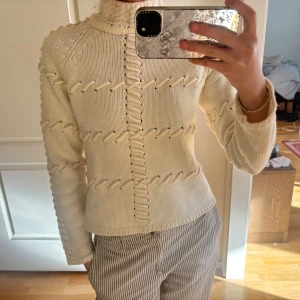 Off-white stickad tröja med unik design - Säljer en off white stickad tröja med en cool och unik design. Tröjan har långa ärmar och ett snyggt mönster av korsade detaljer framtill. Perfekt för att hålla sig varm och stilren under kyligare dagar.