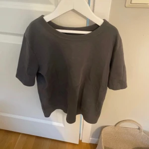 Grå kortärmad t-shirt - Säljer en stilren grå t-shirt med korta ärmar. Perfekt för en avslappnad look. T-shirten har en rund halsringning och är gjord i ett mjukt material.