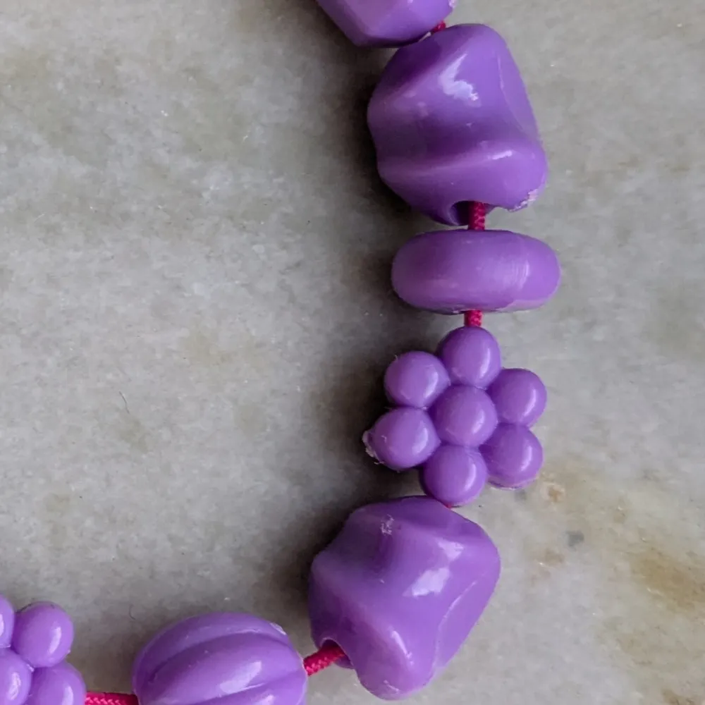Säljer ett sött lila armband med olika former som hjärtan och blommor. Armbandet är trätt på ett rosa snöre och har en lekfull design. Perfekt för att lägga till en färgglad touch till din stil!. Asusteet.