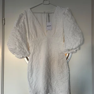 Vit klänning med puffärmar från Showpo - Säljer en elegant vit klänning från Showpo med v-ringning och puffiga ärmar. Klänningen har en fin textur och en figurnära passform som ger en stilren look. Perfekt för speciella tillfällen! Den är endast testat och säljer eftersom jag ska ha en annan som studentklänning 