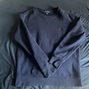 Marinblå tröja från Ralph Lauren - Säljer en marinblå tröja från Ralph Lauren med det klassiska röda broderade logotypen på bröstet. Tröjan har långa ärmar och en rund halsringning. Storlek M i barnstorek men sitter som XS, kom privat för tex mått, flera bilder eller om ni bara undrar något.