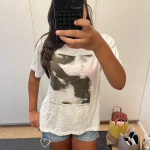 Vit t-shirt med abstrakt tryck - Vit t-shirt med coolt abstrakt tryck i svart och grått framtill. Klassisk passform med korta ärmar och rund hals. Perfekt till jeansshorts eller baggy jeans för en avslappnad vibe.