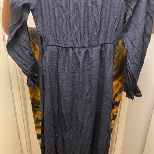 Mörkblå långklänning med omlott - Snygg mörkblå långklänning med omlottdetalj i midjan och långa ärmar med rynkade muddar. Klänningen har en luftig och lite skrynklig look, perfekt för dig som gillar en avslappnad men ändå chic stil.